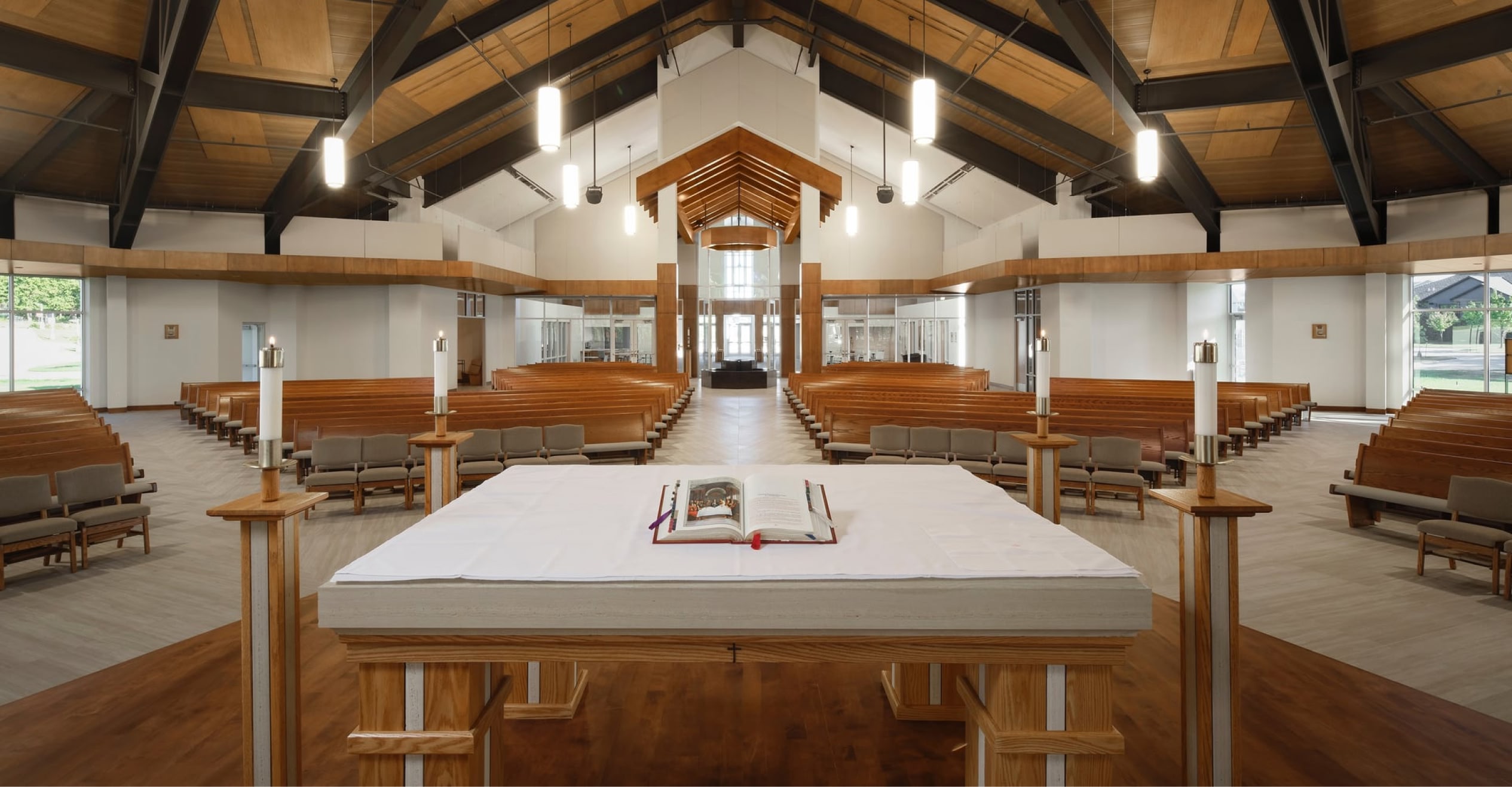 A modern church interior with wooden pews arranged in a semicircle facing a central altar, holding an open book.