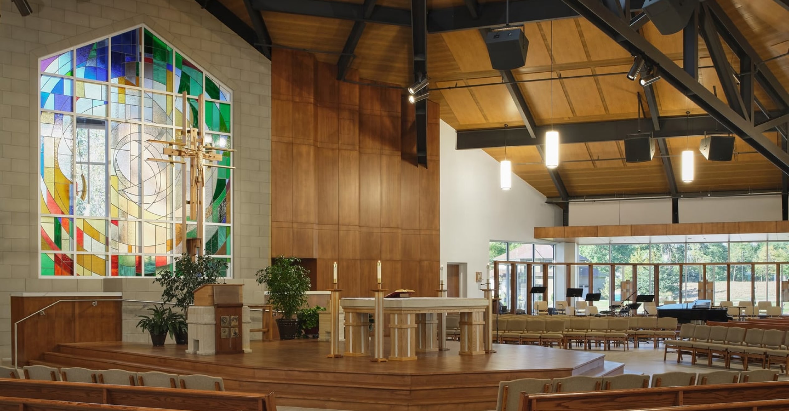 Spacious church interior with modern wooden decor, featuring a colorful stained glass window beside a large crucifix and altar