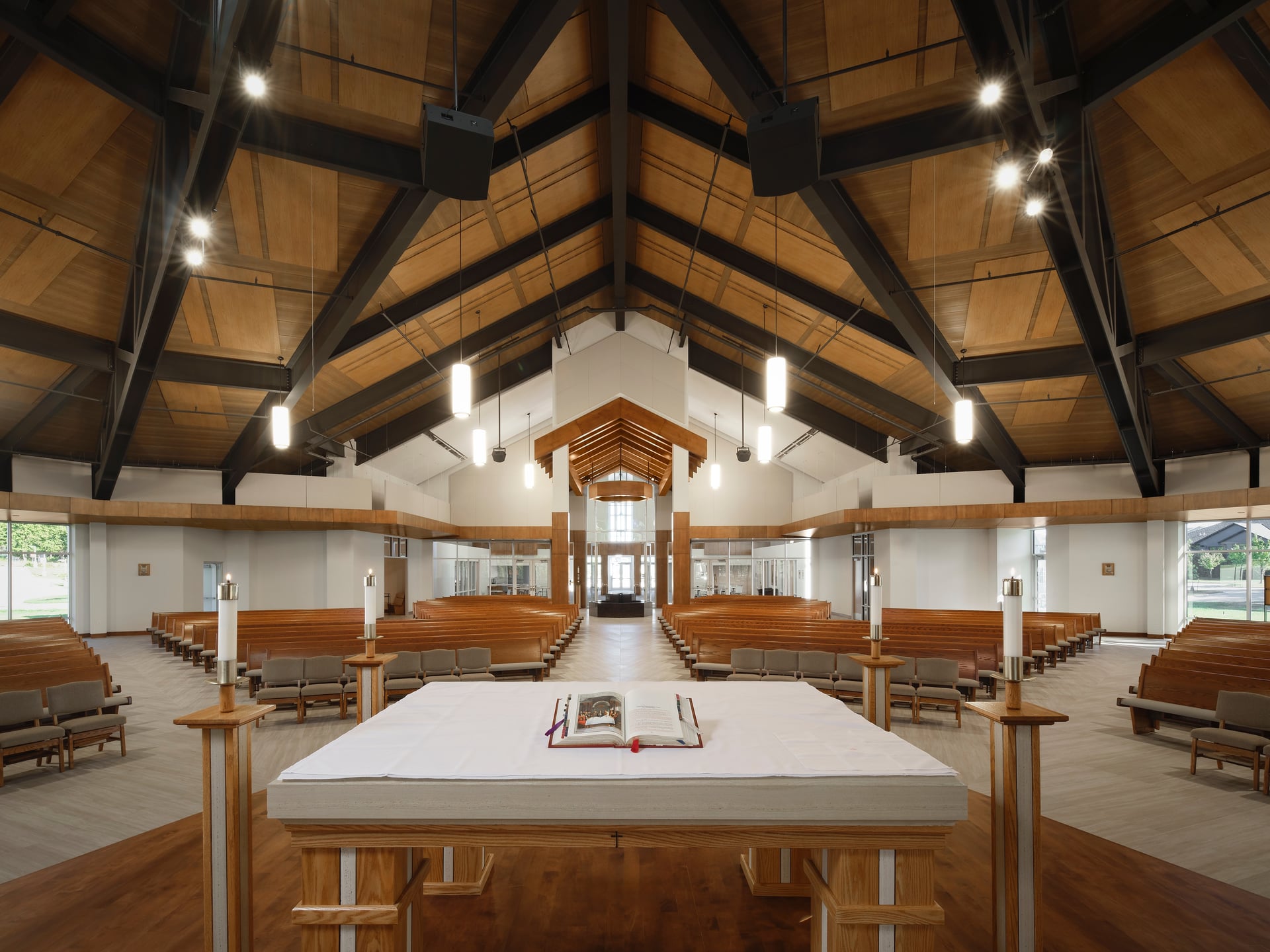 Interior view of St. Thomas More Catholic Church sanctuary showing the altar, wood pews, and vaulted timber ceiling with exposed beams and pendant lighting.