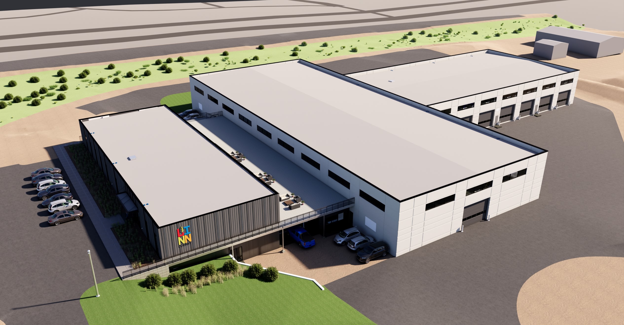 Aerial view of a modern industrial building with a large, white roof and adjacent parking area. Surrounding areas include greenery and additional structures.