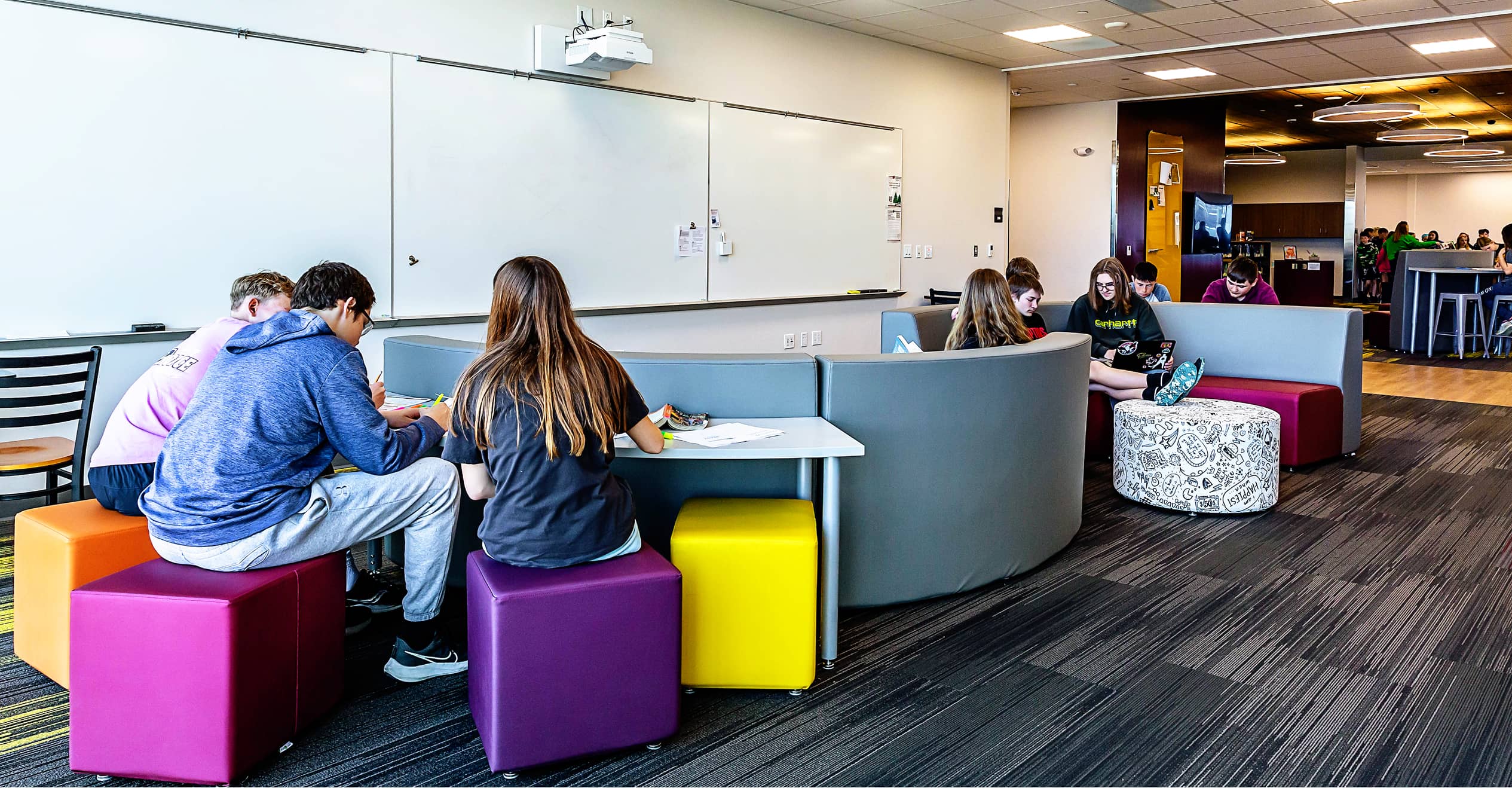 A modern classroom with students seated on colorful cube stools and cushioned benches around tables.