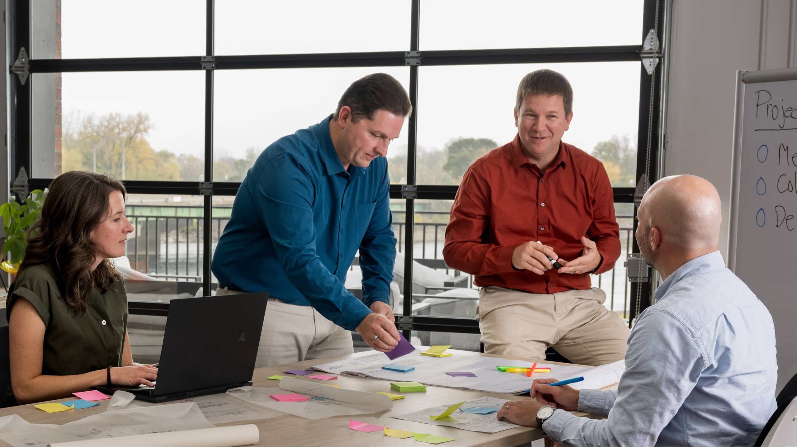 Four people from an architecture firm collaborate in a bright office, gathered around a table with colorful sticky notes during a focused design meeting.