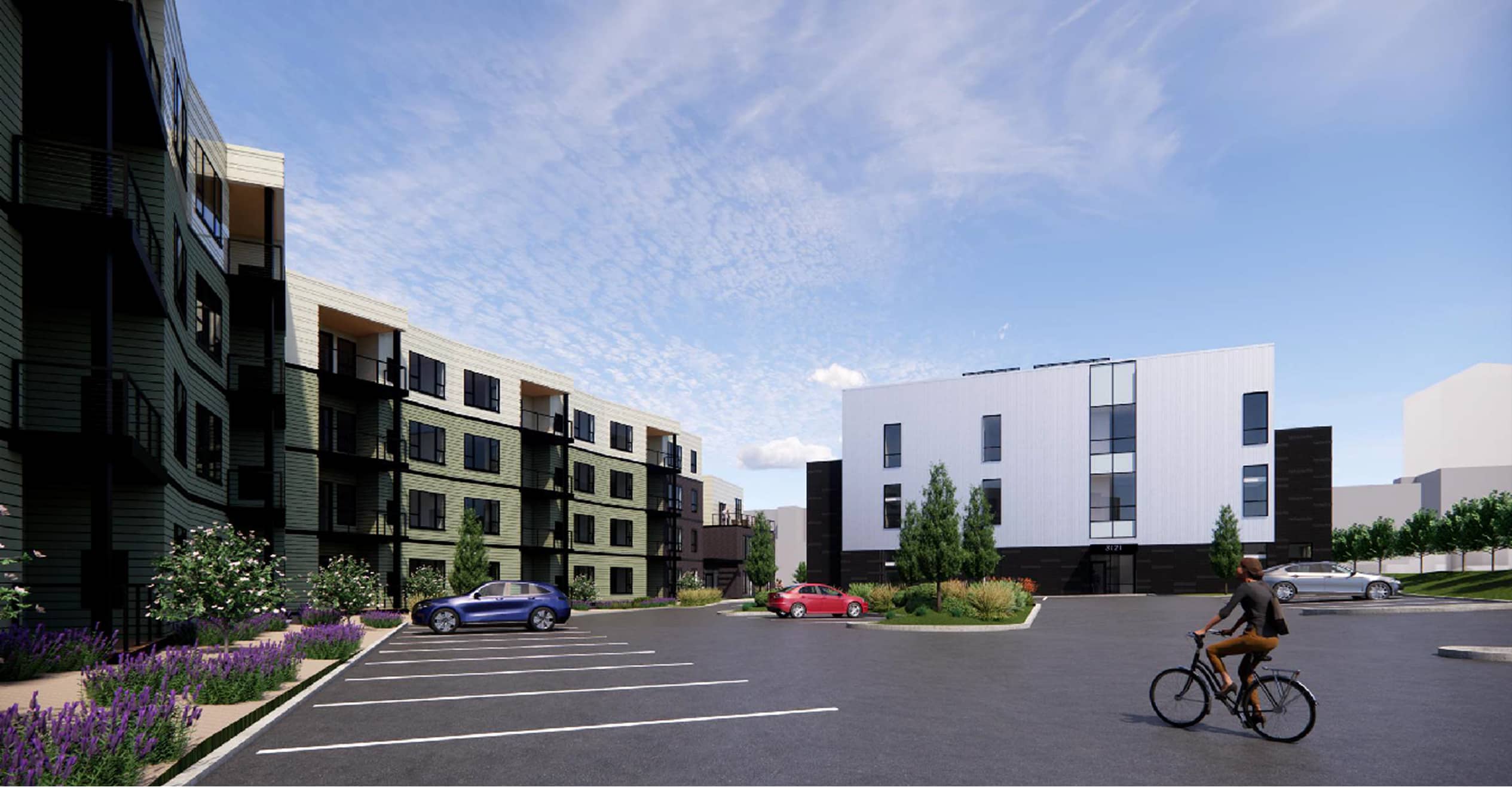 A modern apartment complex with a green and white exterior under a partly cloudy sky. A cyclist rides through an empty parking lot