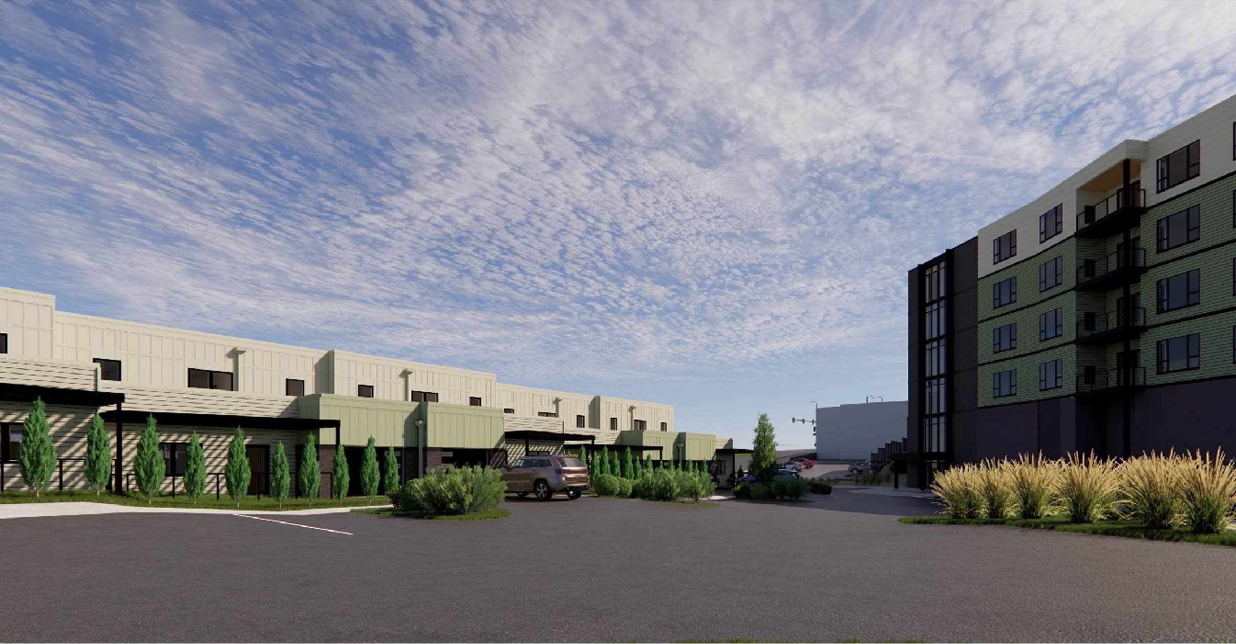 Modern apartment complex under a blue sky with clouds. Buildings have green and beige tones, surrounded by greenery and an open paved area.