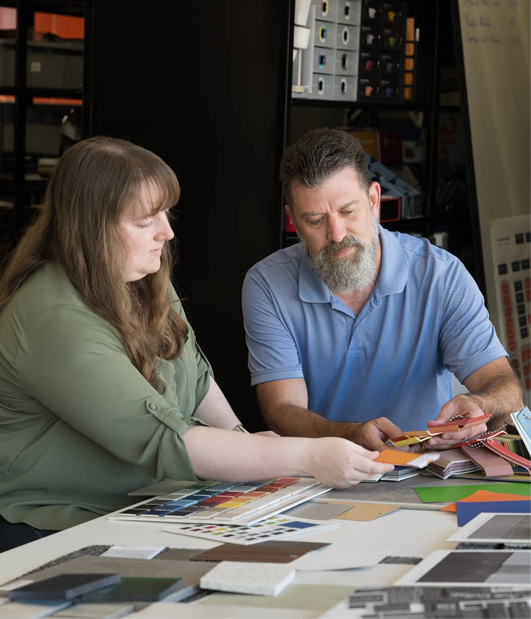 Two people sit at a table covered with color swatches and samples, deeply focused on selecting materials.