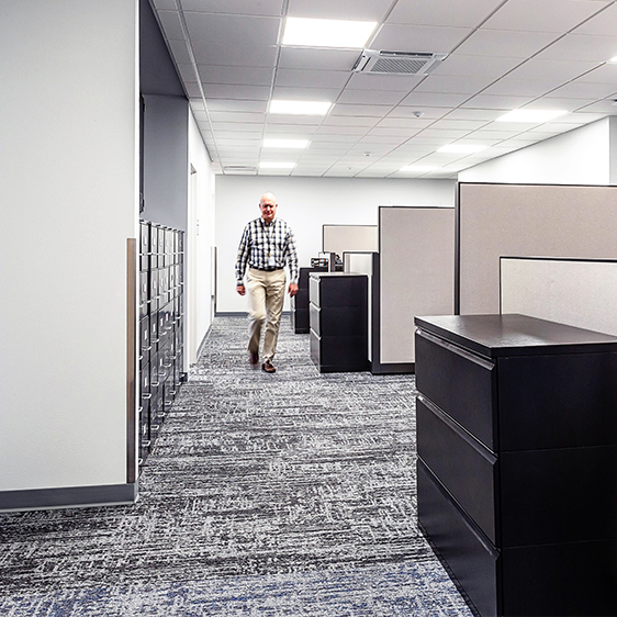 Open office workspace with cubicles and improved circulation, showing a staff member walking through the remodeled Cedar Falls City Hall.