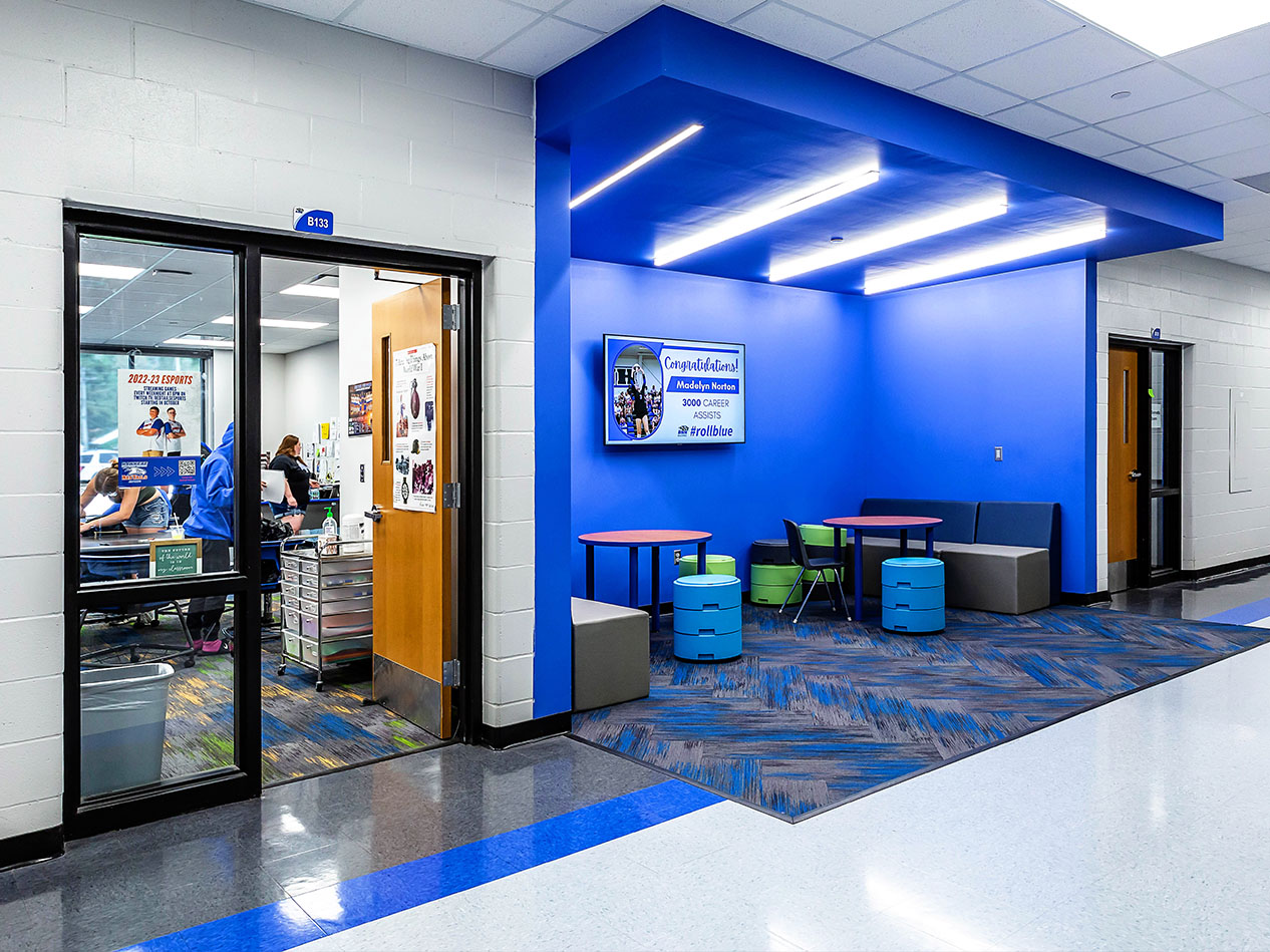 Blue-walled collaboration area with glass doors, stools, and a wall-mounted screen.