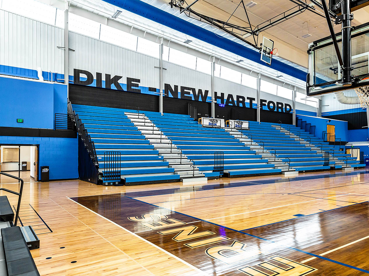 Dike-New Hartford gymnasium with blue bleachers, basketball court, and school branding.