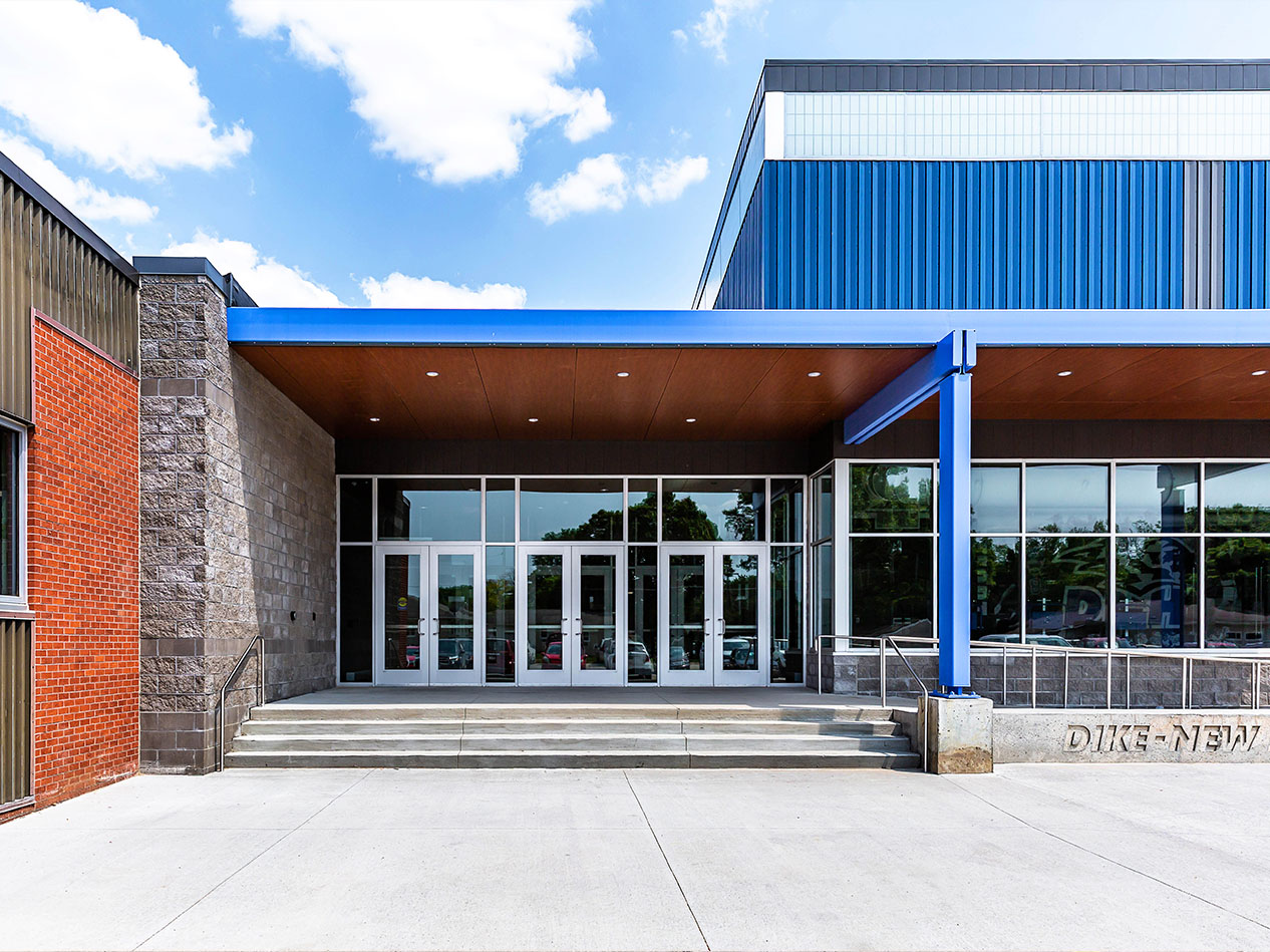 Exterior view of the Dike-New Hartford school entrance with brick facade, blue siding, and glass doors.