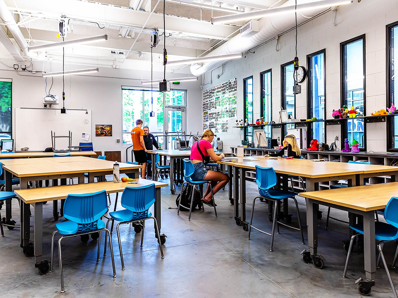 Classroom makerspace with students working at tables and bright blue chairs.