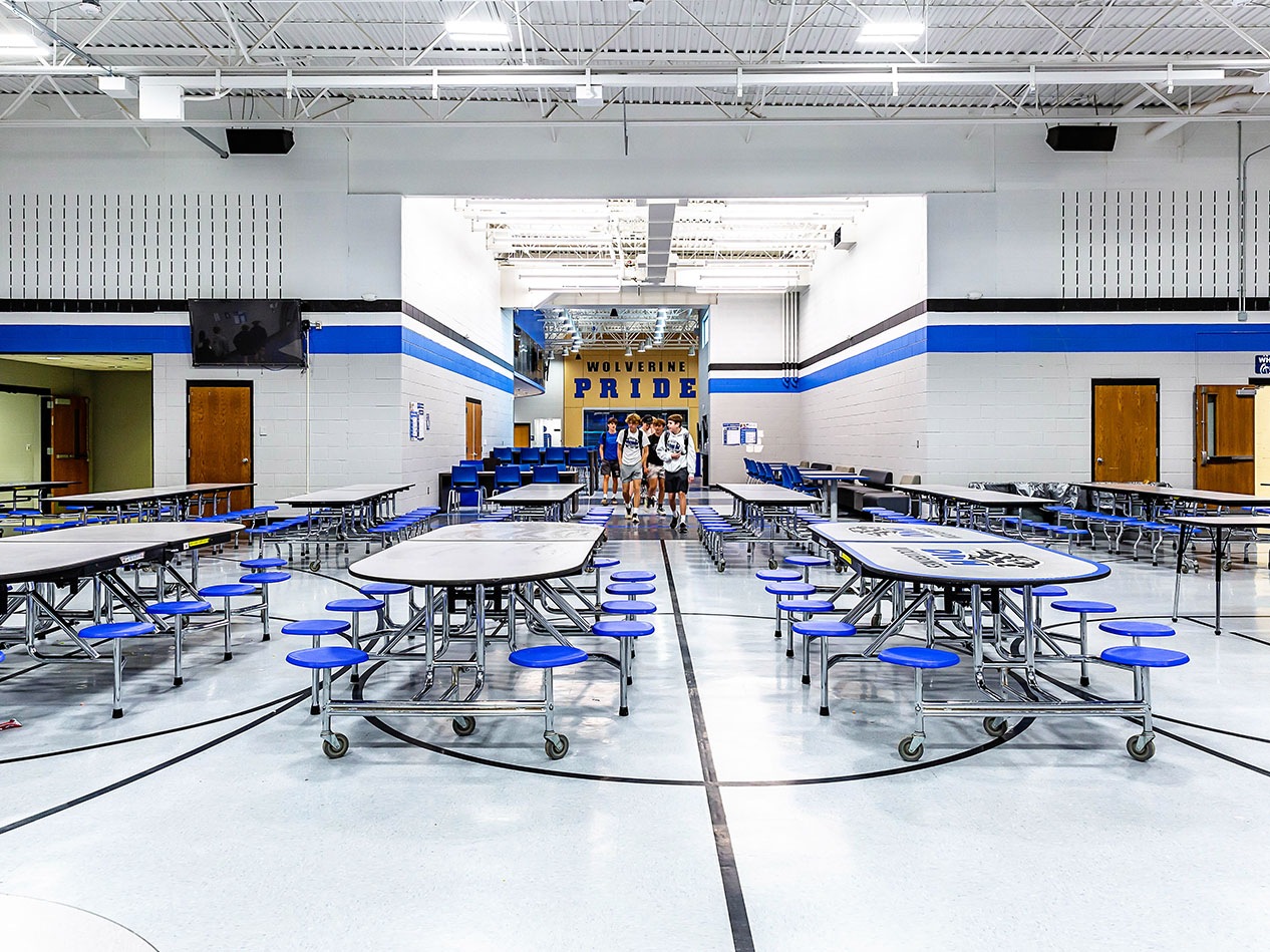 Cafeteria with round tables, blue accents, and Wolverine Pride wall graphics.
