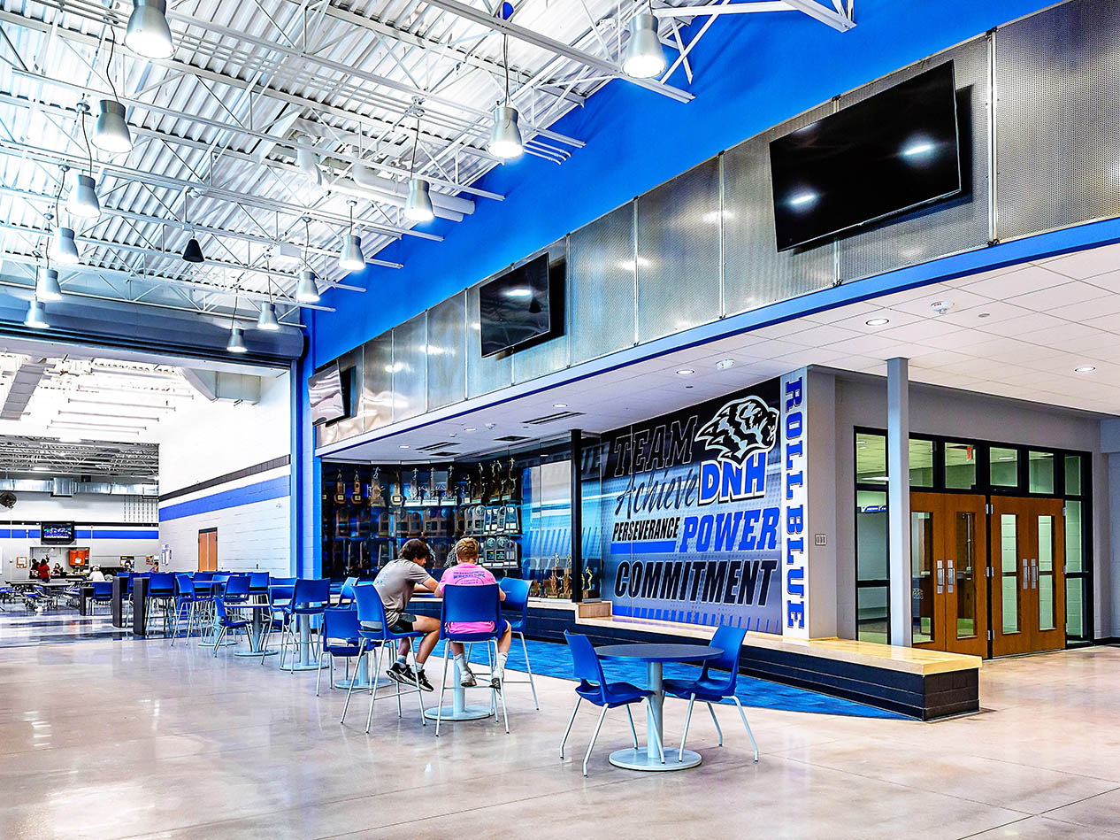 School corridor with blue accent wall, built-in bench seating, and large display screen.