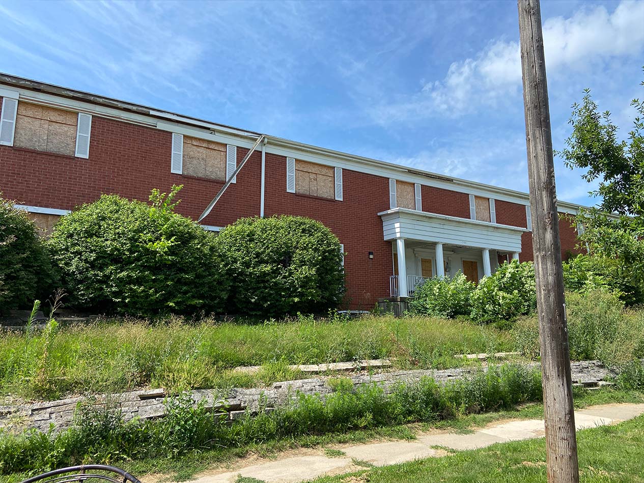 Exterior view of the Colonial Centre building prior to renovation, showing boarded windows, overgrown landscaping, and the original brick facade before conversion to The Heights affordable housing.