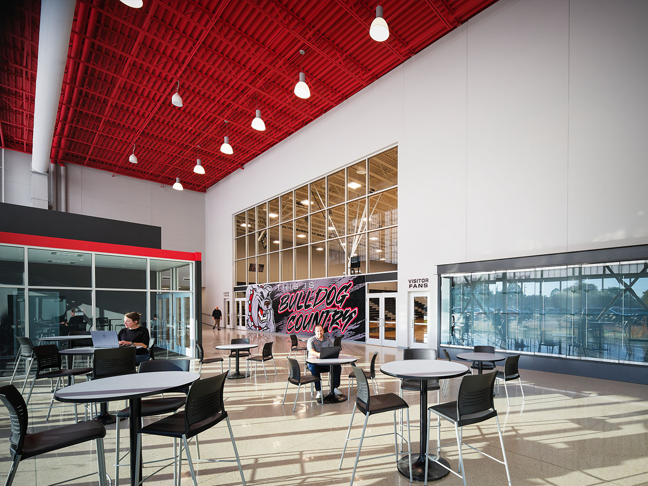 Modern school lobby with red ceiling accents, glass walls, and casual seating.